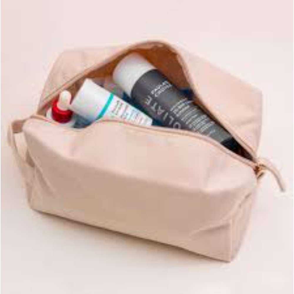 Beige toiletry bag with skincare products on a light pink background