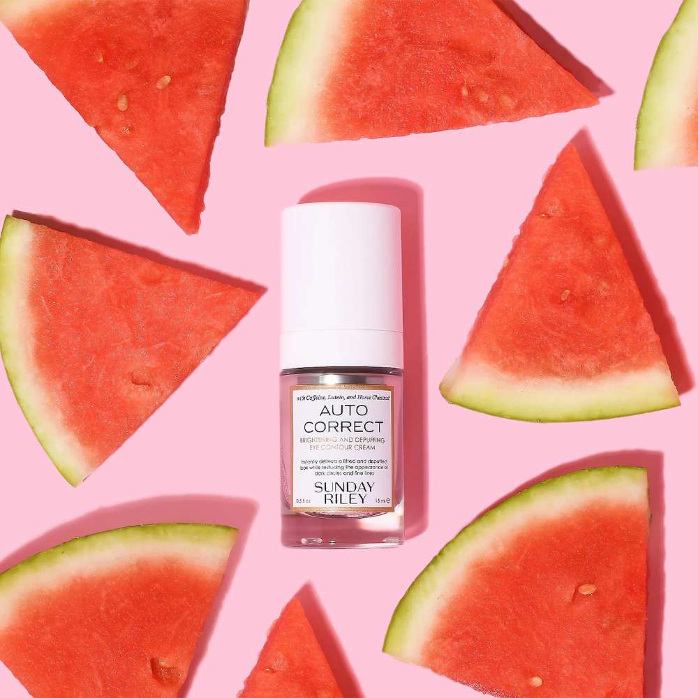 Skincare bottle labeled 'Auto Correct' surrounded by watermelon slices on a pink background