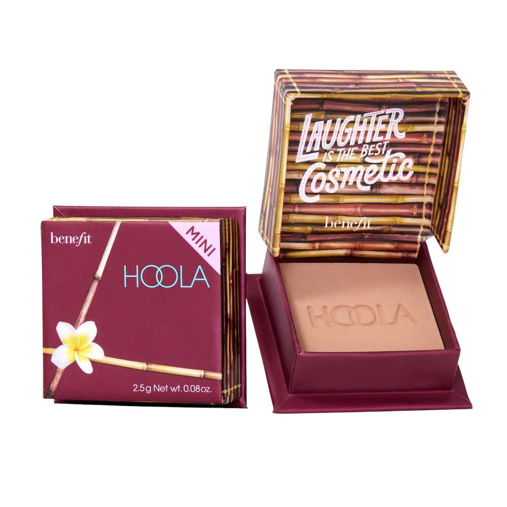 A compact of Benefit Cosmetics Hoola Matte Bronzer with the product name visible on the front. The packaging is purple with a floral design and the product is shown alongside its box lid which has the brand's logo and the word 'Laughter'.